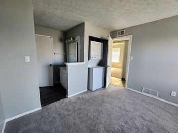 a living room with gray carpet and a kitchen